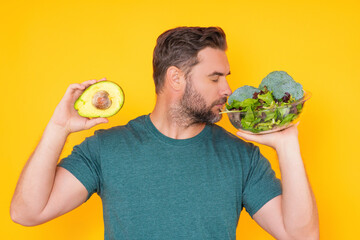 Man hold vegetables, isolated on yellow. Man holding avocado and broccoli vegetables. Cooking vegetables. Dieting, bowl with salad. Green salad. Healthy vegan food concept. Fresh vegetables.