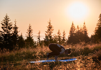 Sporty woman doing crow pose in the morning. Young woman meditating at summer dawn. Meditation in mountains.
