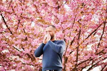 Man allergic suffering from seasonal allergy at spring in blossoming garden at springtime. Man...