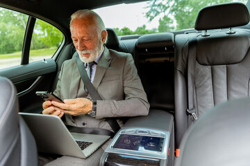 Elderly businessman checking his smartphone while traveling in a luxury sedan