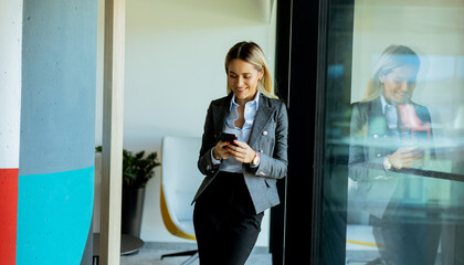 Businesswoman reading messages on smartphone in modern office, daytime reflection