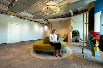 Modern office lounge with green circular seating and woman working on laptop during daytime