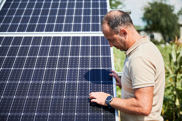 Adult man controling operation of solar cells. Male looking at his new solar panel. Man checking...