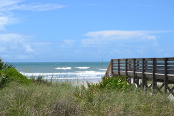 A scenic view of the wooden walkway leading to the turquoise waters and horizon behind the dunes at Ponce Inlet Beach Florida