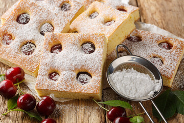 Fruity cherry cake known as Bublanina sprinkled with powdered sugar closeup on the parchment on the wooden table. Horizontal