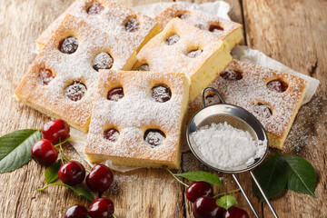 Bublanina Czech and Slovakian Cherry Bubble Cake with sprinkled with powdered sugar closeup on the parchment on the wooden table. Horizontal