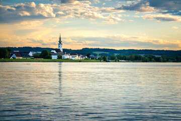 Naklejka premium Sunset on the Danube river with a small town and a church tower on the shore photographed from the water