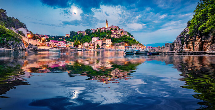 Illuminated old building of Vrbnik  port reflected in the calm waters of Adriatic sea. Picturesque summer seascape of Krk island, Kvarner bay archipelago, Croatia, Europe. Travel the world..