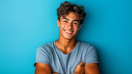 Obraz premium A young man smiles before the blue wall as he crosses his arms for the photo