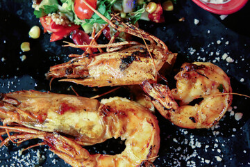 Prawns Shrimps roasted on pan with tamato and salad on dark rustic background. top view.