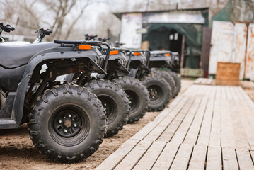 Row of quad bikes parked outside rental service, closeup photo. Outdoor adventure: Several quad...