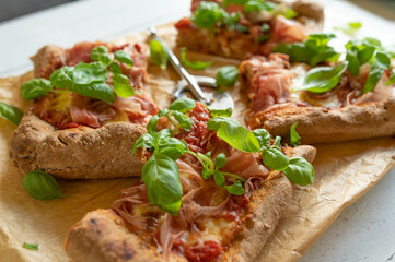 Whole wheat pizza with italian raw ham, mozzarella cheese and basil leaves