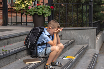 Frustrated child with learning difficulties. he sits on the steps by the school and covers his face...