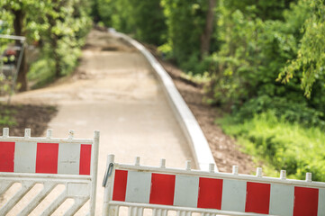 Rot-weiße Absperrgitter an Baustelle Hochwasserschutz mit Damm an Uferweg mit Sträuchern und Bäumen