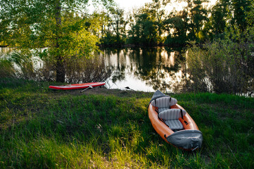 an inflatable boat and a board are lying on the grass on the shore of the lake