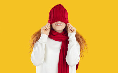 Funny teenage girl in scarf behaves cheerfully and playfully, pulling red warm hat on her eyes....