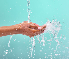 Fototapeta premium Studio, water drops and hands of woman for wellness with cleaning, bacteria prevention and skincare hydration. Dermatology, liquid splash and model cupping palm for shower or bath by blue background