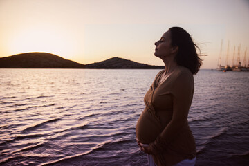 Pregnant woman on the shore of a lagoon at sunset. The breeze comforts her