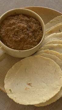 Homemade corn tortillas made with nixtamalized corn flour. Veracruz-style thick sauce made with dried chilies, pumpkin seeds, and unhulled sesame seeds. Mexican meal. Table spin. Vertical video.
