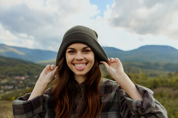 A stylish woman in a plaid shirt and beanie admiring the majestic mountains in a fashion travel...
