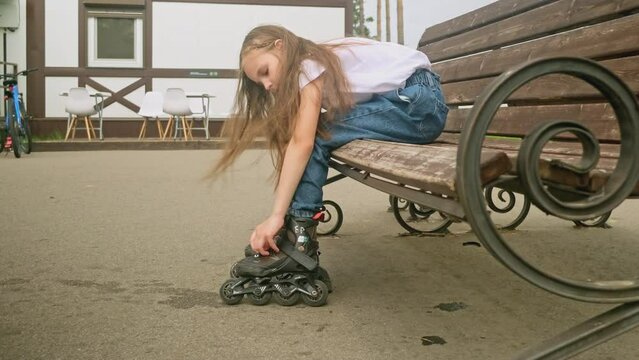little girl to put on roller skates while sitting outdoors on street bench