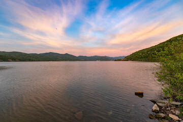 A serene sunset over a tranquil lake with rippled water, mountains in the distance, and a clear sky...