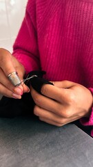 Female teen girl learning to sew by hand with needle and thimble, scrap of black fabric,pink sweater