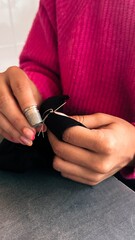 Female teen girl learning to sew by hand with needle and thimble, scrap of black fabric,pink sweater