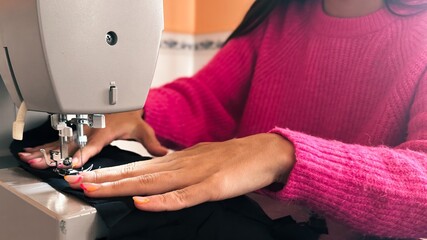 Young woman learning to sew at home with scraps of black fabric, woman with young sweater, sewing