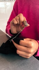 Female teen girl learning to sew by hand with needle and thimble, scrap of black fabric,pink sweater
