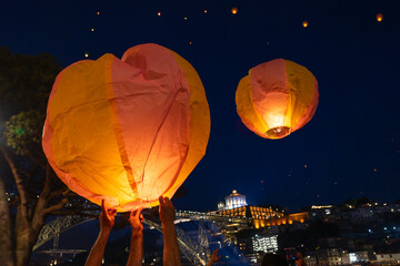 Festa de Sao Joao do Porto flying lanterns with hands of people in Porto Portugal at st John's eve next to duoro river bank