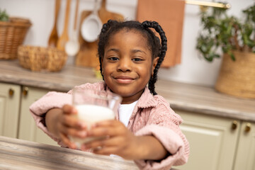 Happy African American kid drinking milk in kitchen