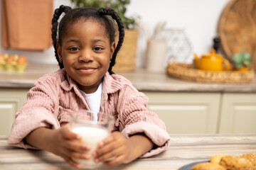 Happy African American kid drinking milk with cookies in kitchen