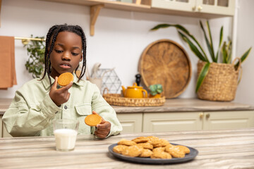 Joyful little girl enjoying delicious snack at home drinking milk with cookies