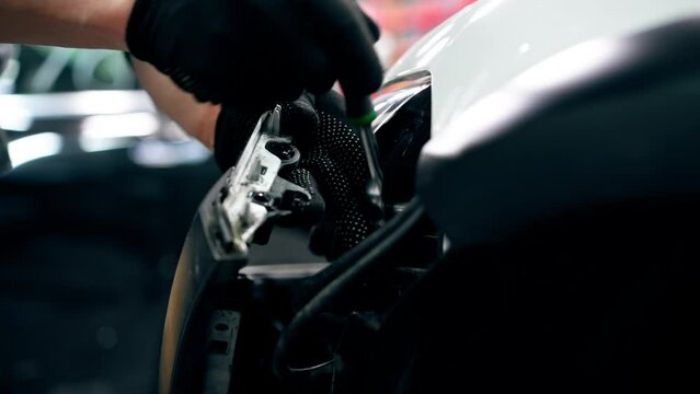 close-up At a service station master auto mechanic unscrews the bolts to remove the headlight