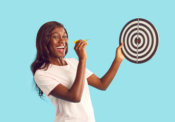 Portrait of a young overjoyed happy african american woman in casual clothes aiming dart arrow at...