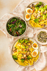Delicious breakfast, pasta with fried mushrooms and broccoli, green peas and corn, fresh mix salad with radishes with seeds, top view