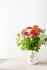 Summer bouquet of colorful Zinnia, onion inflorescences and mint sprigs, bouquet of flowers on the table near the wall, home decoration with flowers