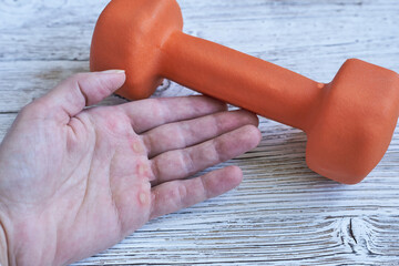Female hand with calluses and dumbbell on wooden background. Close-up.