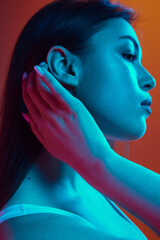 Profile view of young beautiful woman posing in neon light highlighting elegant lines of her face...
