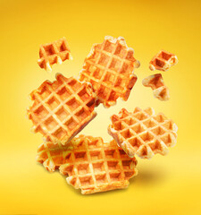 Belgian waffles and waffle pieces levitating in air on yellow background. File contains clipping paths.