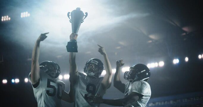 Diverse American Football Team Members Raise the Championship Cup. Happy College Team Standing Under Stadium Lights, Celebrating a Triumphant Victory in Front of a Crowded Stadium with Fans - Powered by Adobe