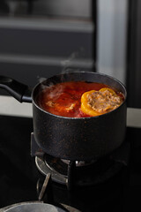 Stuffed peppers with meat and rice cooking in a pot on the stove in red tomato sauce. Sauce is bubbling and steaming, creating a delicious and appetizing food scene. 