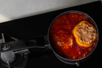 Stuffed peppers with meat and rice cooking in a pot on the stove in red tomato sauce. Sauce is bubbling and steaming, creating a delicious and appetizing food scene. 