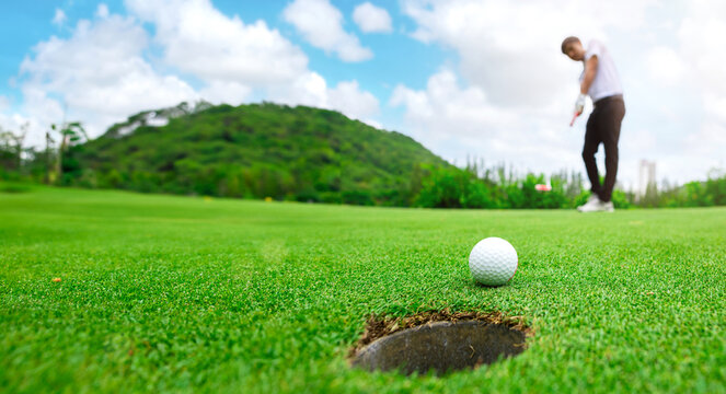 Golfer is using a putter to put a golf ball on the green.