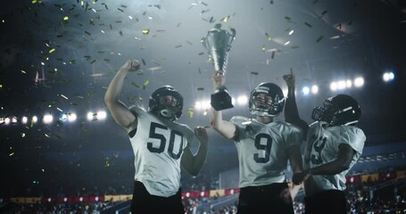 Joyful American Football Players Excited After Winning a Championship Match Trophy. Diverse Group of Athletes Standing Stadium Under Falling Confetti, Lifting the Cup in the Air
