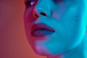 Close up of full, plump female lips with neutral beige lipstick in neon light against gradient background. Facial care procedures. Concept of beauty and care, cosmetology, wellness, spa treatments. Ad
