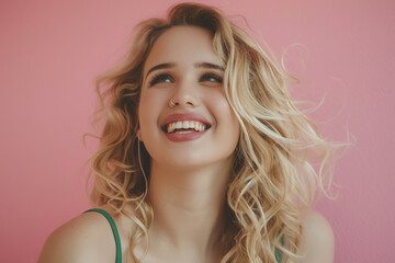 Portrait of beautiful blonde woman with long hair laughing and smiling, wearing green top over pink background