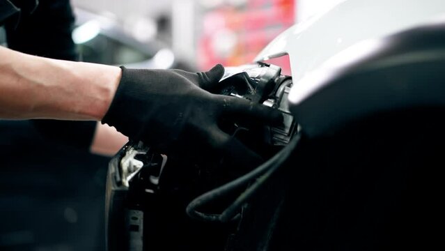 close-up At a service station master auto mechanic disconnects the headlight from the car