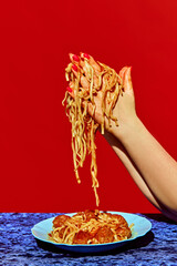 Female hands holding spaghetti with meatballs on plate against red background. Delicious meal and...